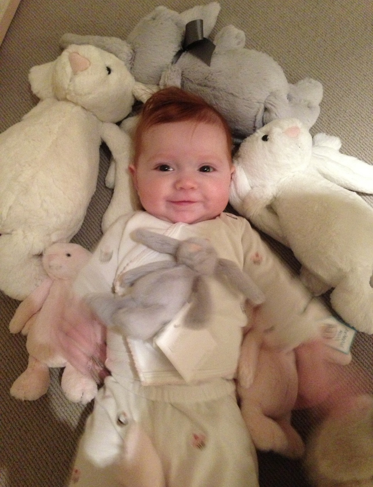 Margot as a baby, smiling, surrounded by stuffed rabbits.