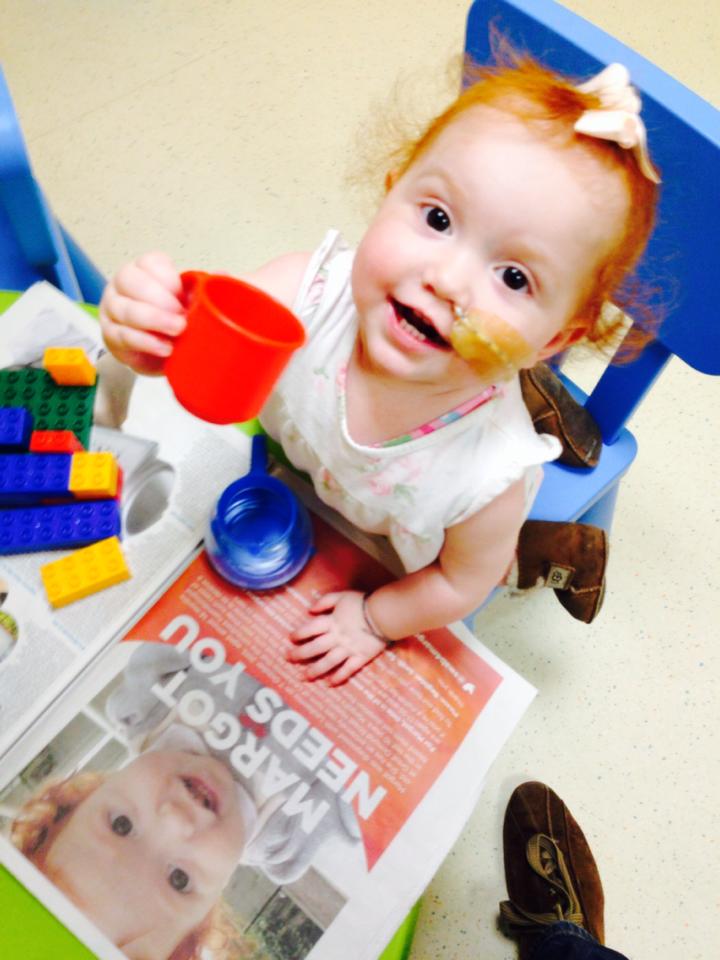 Margot at a small table with a newspaper headline MARGOT NEEDS YOU.